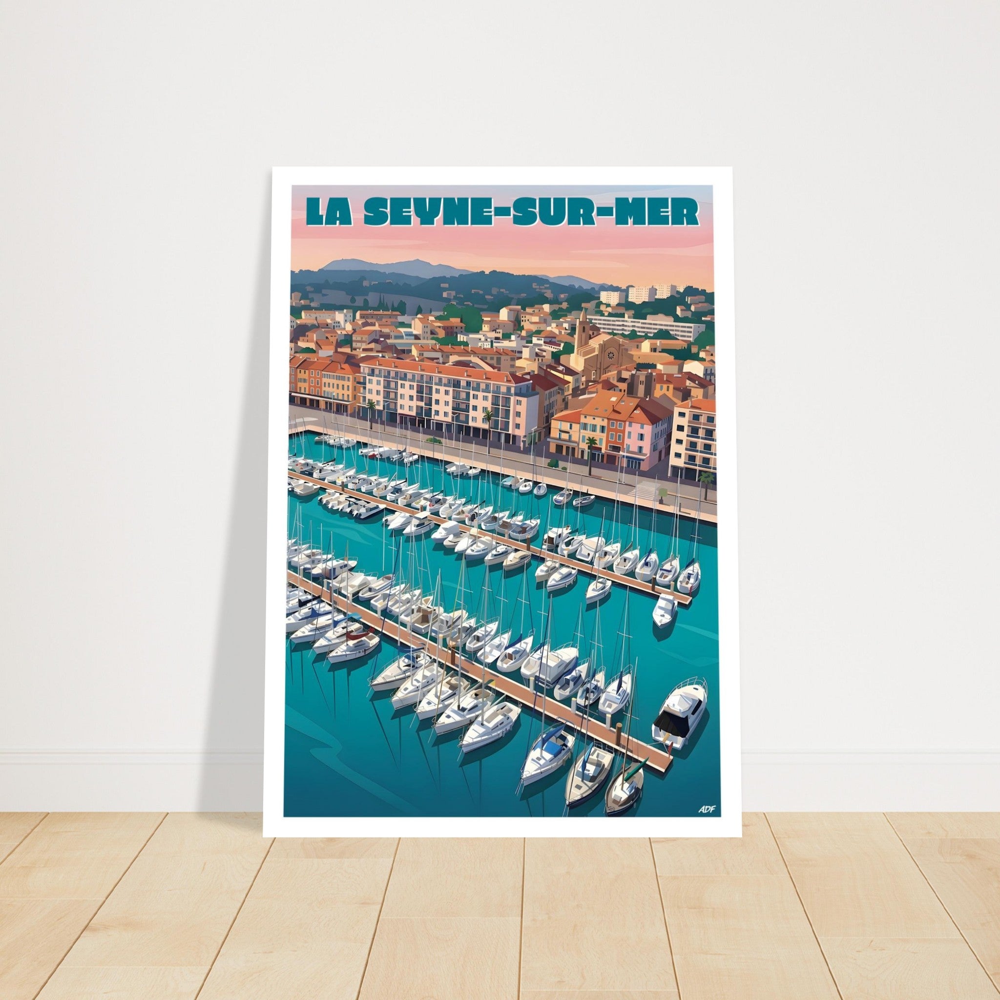 Grand poster encadré de La Seyne-sur-Mer posé au sol sur parquet en bois contre un mur blanc